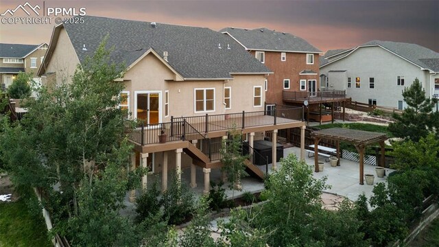 10489 Cedar Breaks Dr, Peyton, CO 80831 - back of house at dusk featuring stairs, a wooden deck, a patio area, stucco siding, and roof with shingles