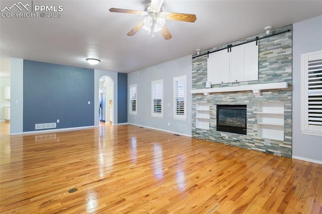 10489 Cedar Breaks Dr, Peyton, CO 80831 - unfurnished living room featuring a ceiling fan, arched walkways, light wood-style flooring, a barn door, and a stone fireplace