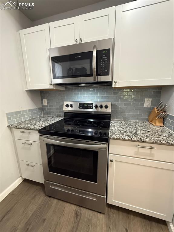 5926 Wisteria Dr, Colorado Springs, CO 80919 - kitchen with appliances with stainless steel finishes, dark wood-style flooring, white cabinets, tasteful backsplash, and light stone counters
