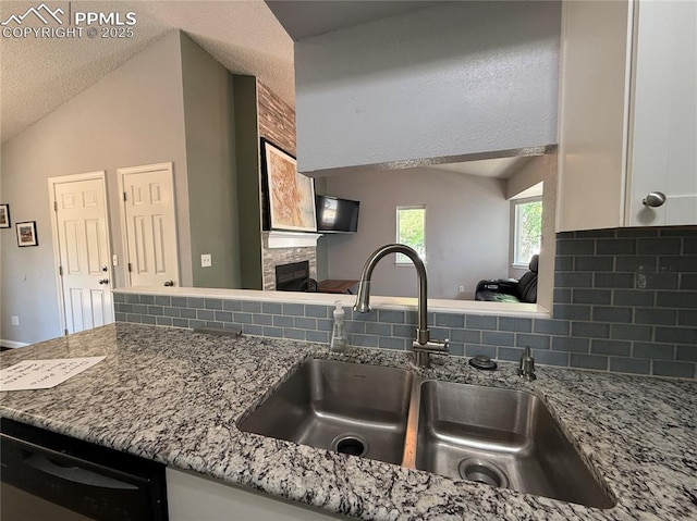 5926 Wisteria Dr, Colorado Springs, CO 80919 - kitchen featuring decorative backsplash, a glass covered fireplace, dishwasher, white cabinetry, and light stone counters