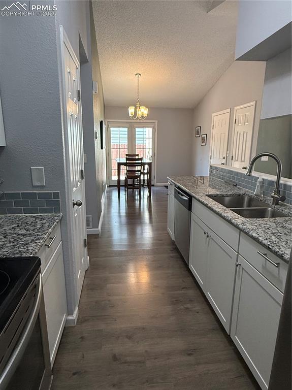 5926 Wisteria Dr, Colorado Springs, CO 80919 - kitchen with stainless steel appliances, dark wood-style floors, a chandelier, a textured ceiling, and hanging light fixtures