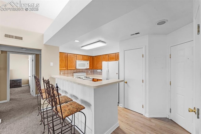 3692 Iguana Dr, Colorado Springs, CO 80910 - kitchen featuring white appliances, a peninsula, light countertops, a breakfast bar, and decorative backsplash