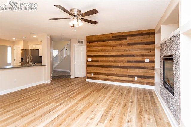 7292 Gardenstone Dr, Colorado Springs, CO 80922 - unfurnished living room with stairway, a glass covered fireplace, wooden walls, ceiling fan, and light wood-style floors