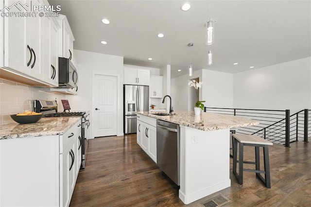 8309 Tom Ketchum Dr, Colorado Springs, CO 80908 - kitchen with appliances with stainless steel finishes, dark wood-style floors, white cabinetry, a breakfast bar, and recessed lighting