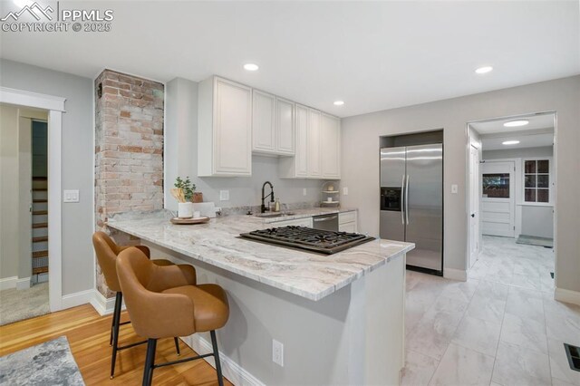 122 E Jefferson St, Colorado Springs, CO 80907 - kitchen featuring appliances with stainless steel finishes, light stone countertops, a peninsula, a kitchen bar, and white cabinets