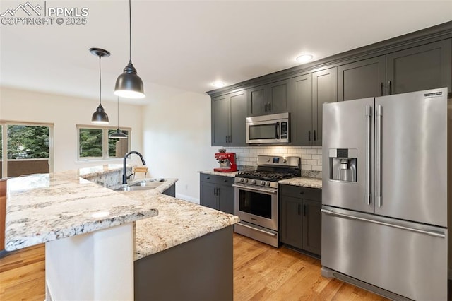 3219 W Pikes Peak Ave, Colorado Springs, CO 80904 - kitchen featuring appliances with stainless steel finishes, backsplash, a kitchen island with sink, light wood-style floors, and light stone countertops