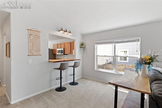 6534 Harvey Ln, Colorado Springs, CO 80923 - kitchen featuring light carpet, stainless steel microwave, a kitchen bar, and brown cabinetry