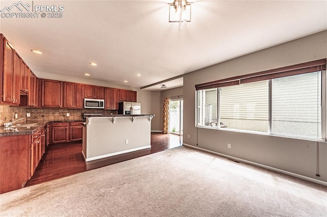 2513 Gilpin Ave, Colorado Springs, CO 80910 - kitchen featuring appliances with stainless steel finishes, dark colored carpet, a breakfast bar, dark countertops, and a kitchen island