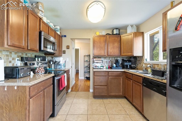 614 Bickley St, Colorado Springs, CO 80911 - kitchen featuring stainless steel appliances, light countertops, backsplash, brown cabinets, and light tile patterned floors