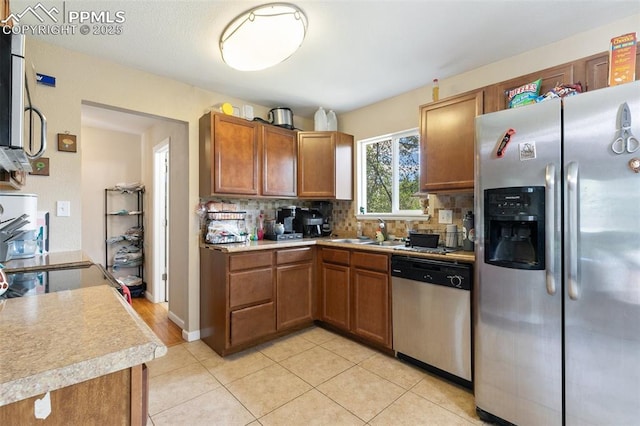 614 Bickley St, Colorado Springs, CO 80911 - kitchen with appliances with stainless steel finishes, decorative backsplash, brown cabinetry, light countertops, and light tile patterned flooring