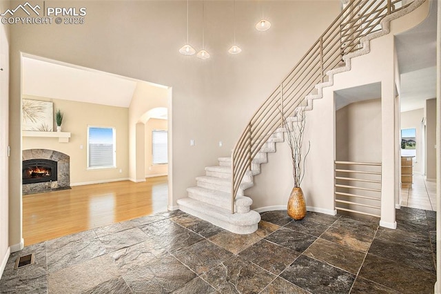 19170 Lochmere Ct, Monument, CO 80132 - entryway with stairs, stone tile floors, a high ceiling, a lit fireplace, and arched walkways