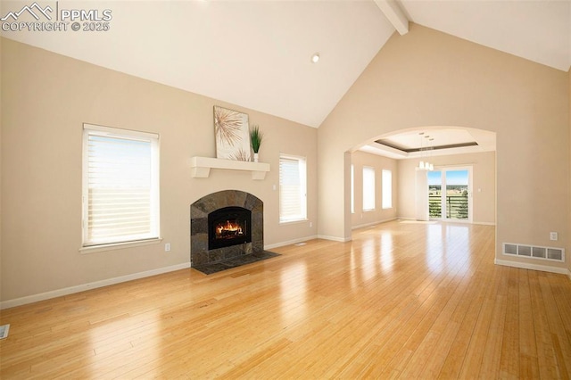19170 Lochmere Ct, Monument, CO 80132 - unfurnished living room with beam ceiling, a fireplace, light wood-style floors, arched walkways, and a chandelier