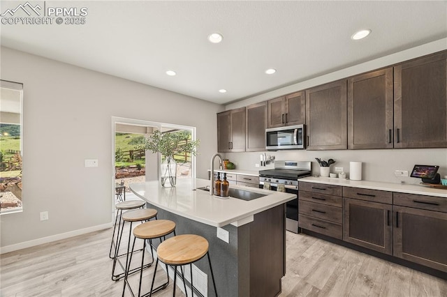 5446 Mesa Top Dr, Monument, CO 80132 - kitchen featuring appliances with stainless steel finishes, a breakfast bar, light wood-style floors, light countertops, and dark brown cabinets
