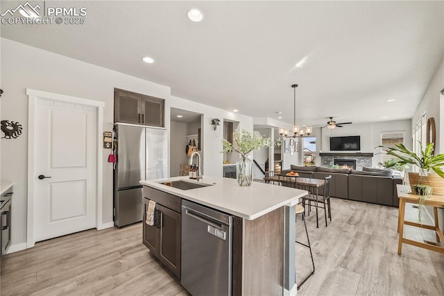 5446 Mesa Top Dr, Monument, CO 80132 - kitchen featuring appliances with stainless steel finishes, a stone fireplace, light wood-style flooring, a kitchen island with sink, and light countertops