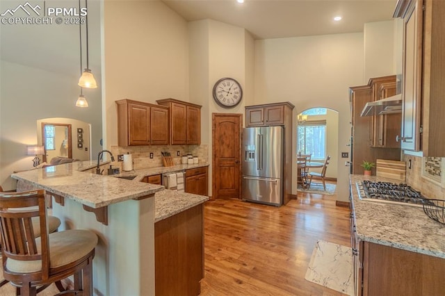 15324 Pole Pine Pt, Colorado Springs, CO 80908 - kitchen with appliances with stainless steel finishes, a peninsula, a towering ceiling, light stone counters, and a kitchen bar