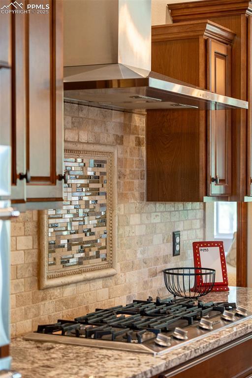 15324 Pole Pine Pt, Colorado Springs, CO 80908 - kitchen with wall chimney range hood, backsplash, stainless steel gas stovetop, and brown cabinetry