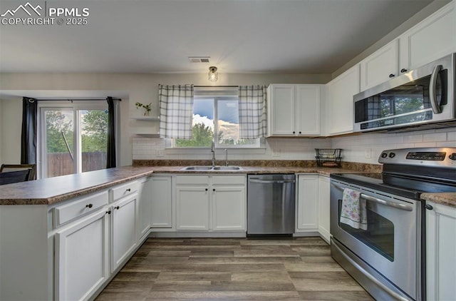 4530 W Jet Wing Cir, Colorado Springs, CO 80916 - kitchen featuring appliances with stainless steel finishes, a peninsula, white cabinets, tasteful backsplash, and dark countertops