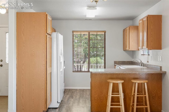 7605 Artisan Pl, Fountain, CO 80817 - kitchen featuring white fridge with ice dispenser, wood finished floors, a breakfast bar, and a peninsula