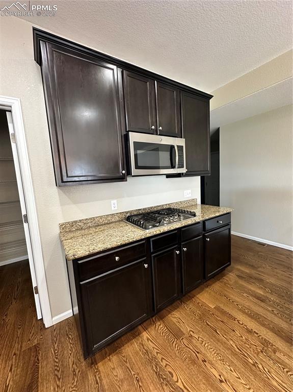 9767 Carnival Ln, Fountain, CO 80817 - kitchen featuring appliances with stainless steel finishes, dark wood-style flooring, a textured ceiling, and light stone countertops