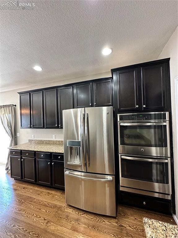 9767 Carnival Ln, Fountain, CO 80817 - kitchen featuring stainless steel appliances, wood finished floors, dark cabinets, a textured ceiling, and recessed lighting