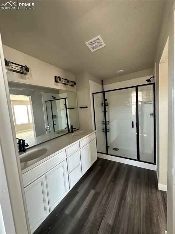 11489 Piping Plover Pl, Colorado Springs, CO 80925 - full bathroom featuring wood finished floors, double vanity, a stall shower, and a textured ceiling