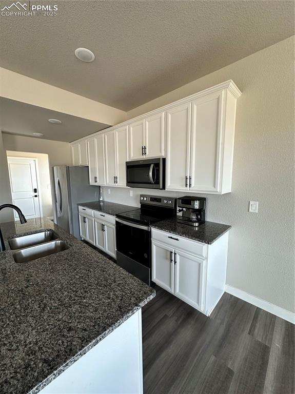 11489 Piping Plover Pl, Colorado Springs, CO 80925 - kitchen with stainless steel appliances, white cabinetry, dark wood-type flooring, dark stone counters, and a textured ceiling