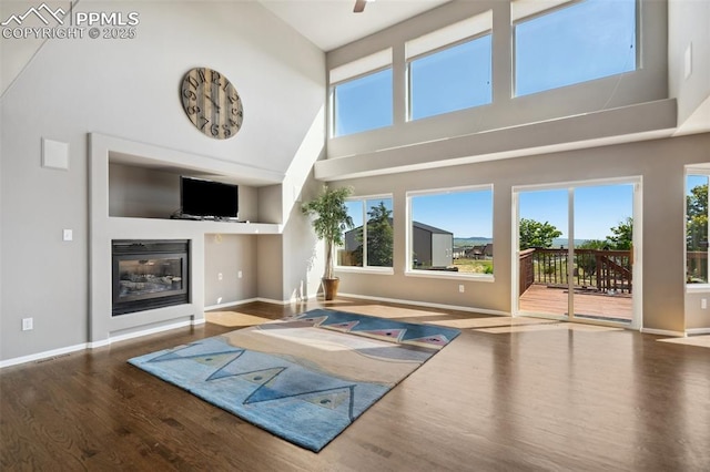 12275 Oregon Wagon Trl, Elbert, CO 80106 - unfurnished living room featuring a towering ceiling, wood finished floors, plenty of natural light, and a glass covered fireplace
