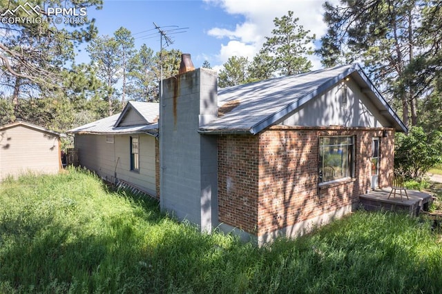 12185 Black Forest Rd, Colorado Springs, CO 80908 - view of home's exterior with a chimney, brick siding, and roof with shingles