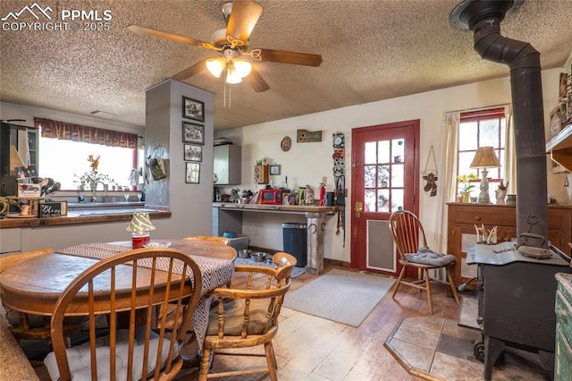 12185 Black Forest Rd, Colorado Springs, CO 80908 - dining space featuring a ceiling fan, a textured ceiling, wood finished floors, and a wood stove