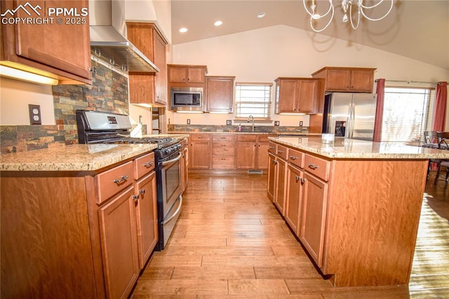 5707 Mark Twain Ln, Pueblo, CO 81008 - kitchen with appliances with stainless steel finishes, wall chimney exhaust hood, light wood finished floors, a kitchen island, and a chandelier
