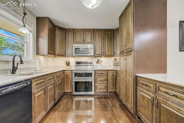 4734 Bunchberry Ln, Colorado Springs, CO 80917 - kitchen with appliances with stainless steel finishes, dark wood-type flooring, light stone counters, hanging light fixtures, and brown cabinetry