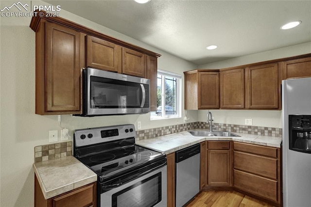 2601 Lynbarton Pt, Colorado Springs, CO 80918 - kitchen with stainless steel appliances, tile countertops, light wood-style flooring, brown cabinets, and tasteful backsplash