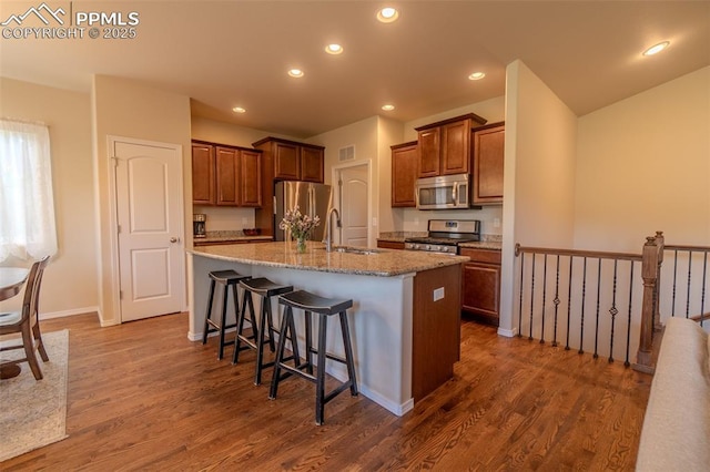 17529 Old Cherokee Trl, Colorado Springs, CO 80921 - kitchen featuring appliances with stainless steel finishes, dark wood-style floors, a kitchen island with sink, light stone countertops, and a kitchen bar