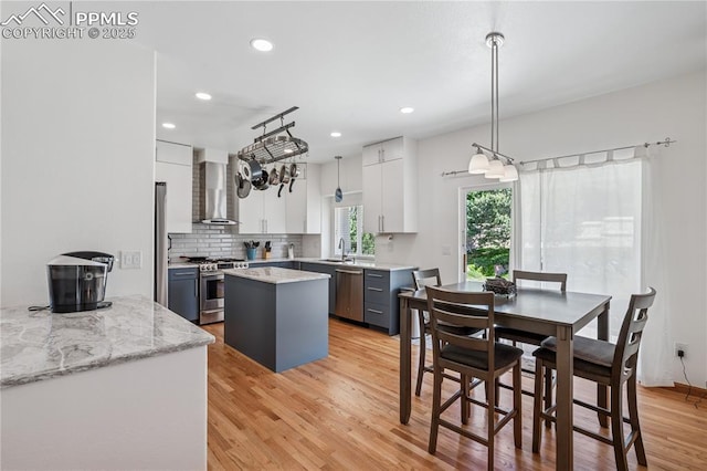 2664 Emerald Ridge Dr, Colorado Springs, CO 80920 - kitchen featuring wall chimney range hood, appliances with stainless steel finishes, a center island, light wood finished floors, and white cabinets