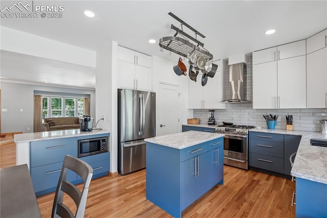2664 Emerald Ridge Dr, Colorado Springs, CO 80920 - kitchen with stainless steel appliances, wall chimney exhaust hood, blue cabinets, a center island, and light wood-type flooring