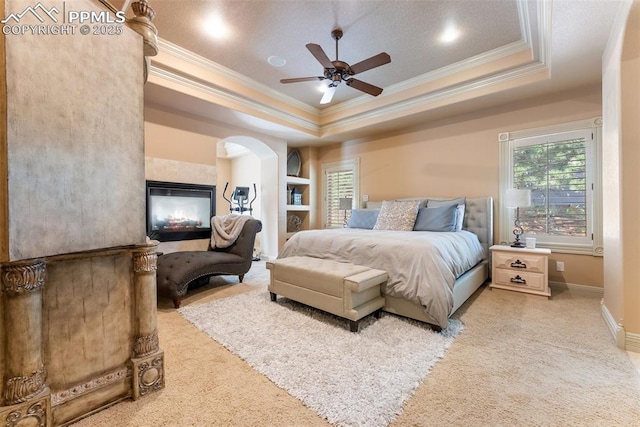2585 Dunfries Ct, Colorado Springs, CO 80919 - bedroom featuring crown molding, a tray ceiling, light colored carpet, arched walkways, and a fireplace