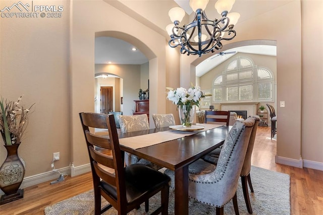 2585 Dunfries Ct, Colorado Springs, CO 80919 - dining area featuring arched walkways, a chandelier, light wood finished floors, a lit fireplace, and vaulted ceiling