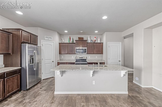 10726 Traders Pkwy, Fountain, CO 80817 - kitchen featuring appliances with stainless steel finishes, wood finished floors, light stone counters, an island with sink, and recessed lighting