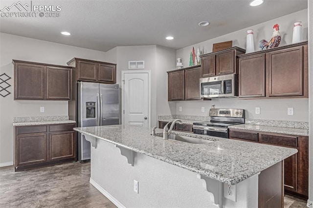 10726 Traders Pkwy, Fountain, CO 80817 - kitchen with stainless steel appliances, a breakfast bar, wood finished floors, dark brown cabinets, and a kitchen island with sink