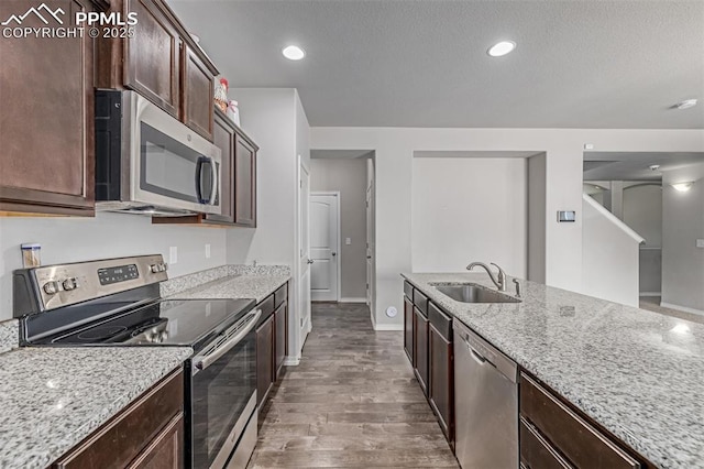 10726 Traders Pkwy, Fountain, CO 80817 - kitchen featuring appliances with stainless steel finishes, wood finished floors, light stone countertops, dark brown cabinetry, and a textured ceiling