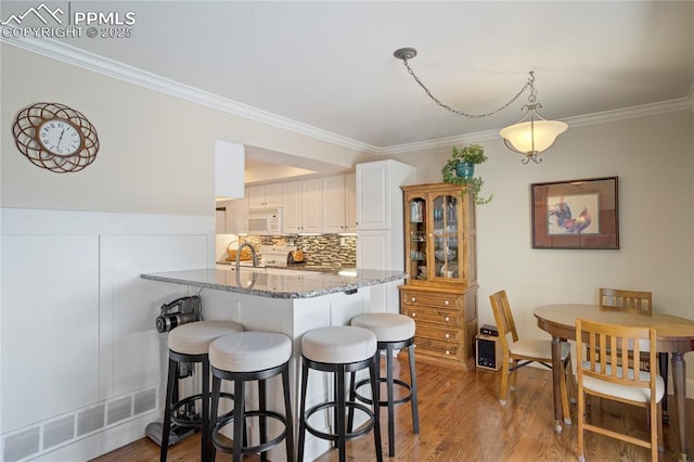 2527 Elite Ter, Colorado Springs, CO 80920 - kitchen with white microwave, a breakfast bar area, light stone counters, crown molding, and light wood-style flooring