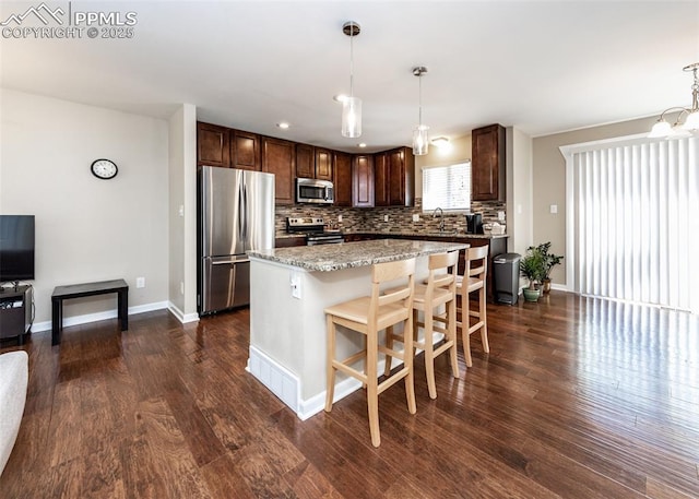 3730 Deep Haven Dr, Colorado Springs, CO 80920 - kitchen with appliances with stainless steel finishes, dark brown cabinetry, dark wood-style floors, tasteful backsplash, and a center island