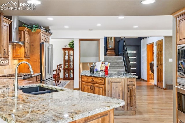 18971 Shadowood Dr, Monument, CO 80132 - kitchen with appliances with stainless steel finishes, wall chimney exhaust hood, light stone counters, light wood-style flooring, and recessed lighting