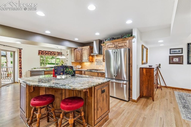 18971 Shadowood Dr, Monument, CO 80132 - kitchen featuring stainless steel appliances, wall chimney exhaust hood, light wood-type flooring, a kitchen island, and light stone counters