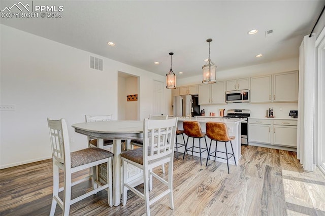 6237 Bodacious Cir, Colorado Springs, CO 80923 - kitchen with appliances with stainless steel finishes, light wood finished floors, recessed lighting, a breakfast bar area, and light countertops