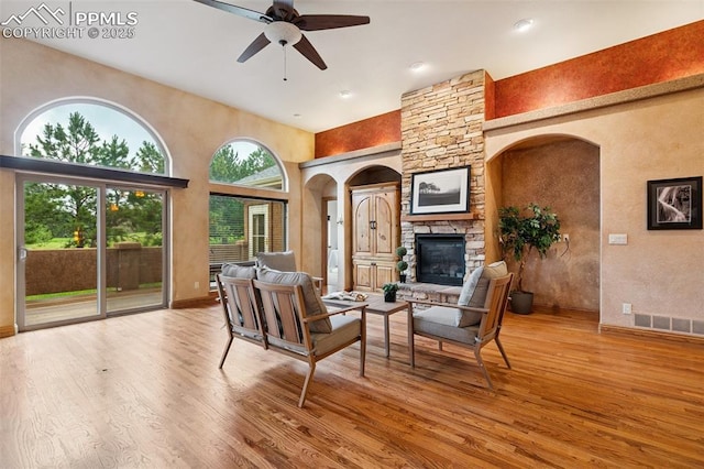 20401 High Pines Dr, Monument, CO 80132 - living room featuring a fireplace, wood finished floors, a ceiling fan, a towering ceiling, and arched walkways