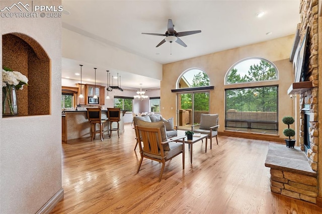 20401 High Pines Dr, Monument, CO 80132 - living room featuring light wood-type flooring, a ceiling fan, a stone fireplace, arched walkways, and a chandelier