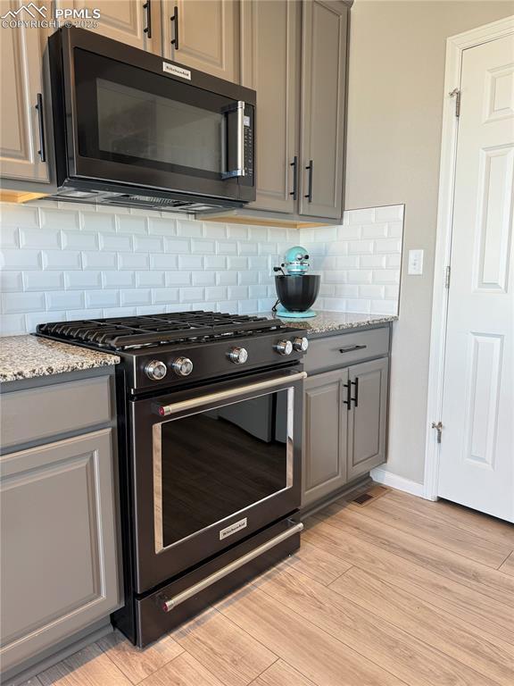 6640 Backcountry Loop, Colorado Springs, CO 80927 - kitchen with gas range oven, black microwave, gray cabinets, and backsplash