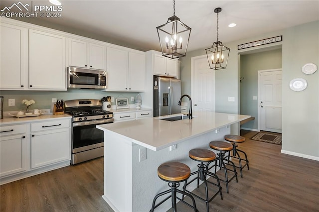 6469 Bodacious Cir, Colorado Springs, CO 80923 - kitchen with appliances with stainless steel finishes, dark wood finished floors, a chandelier, white cabinetry, and a kitchen island with sink