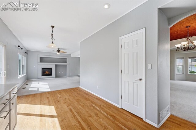 1562 Lookout Springs Dr, Colorado Springs, CO 80921 - unfurnished living room featuring a ceiling fan, built in shelves, arched walkways, a glass covered fireplace, and light wood-style flooring